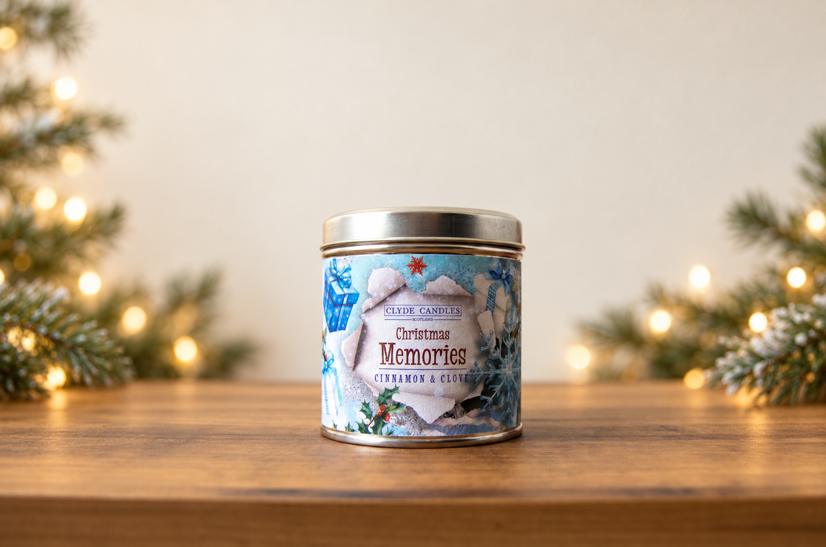 Clyde Candles Christmas Memories Cinnamon & Clove candle tin on a wooden table with evergreen branches and warm Christmas lights