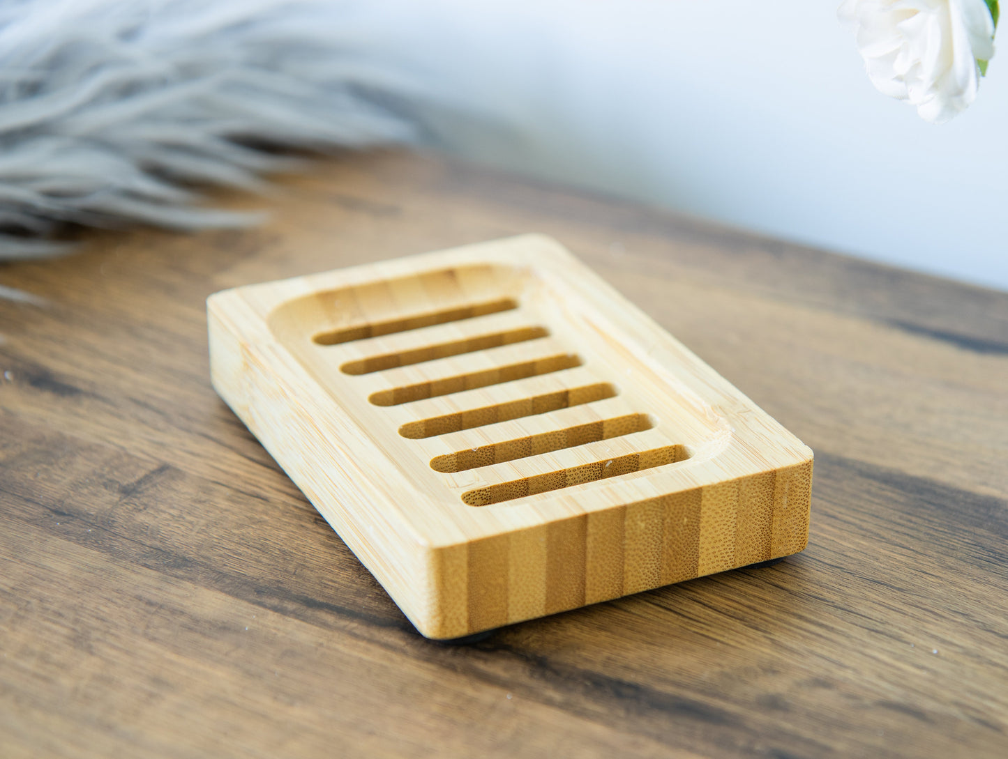A natural brown bamboo soap dish with drainage holes, placed on a wooden surface.