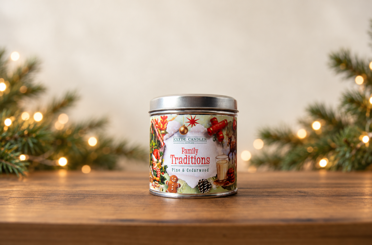 Clyde Candles Family Traditions Pine & Cedarwood candle tin on a wooden table with evergreen branches and warm Christmas lights